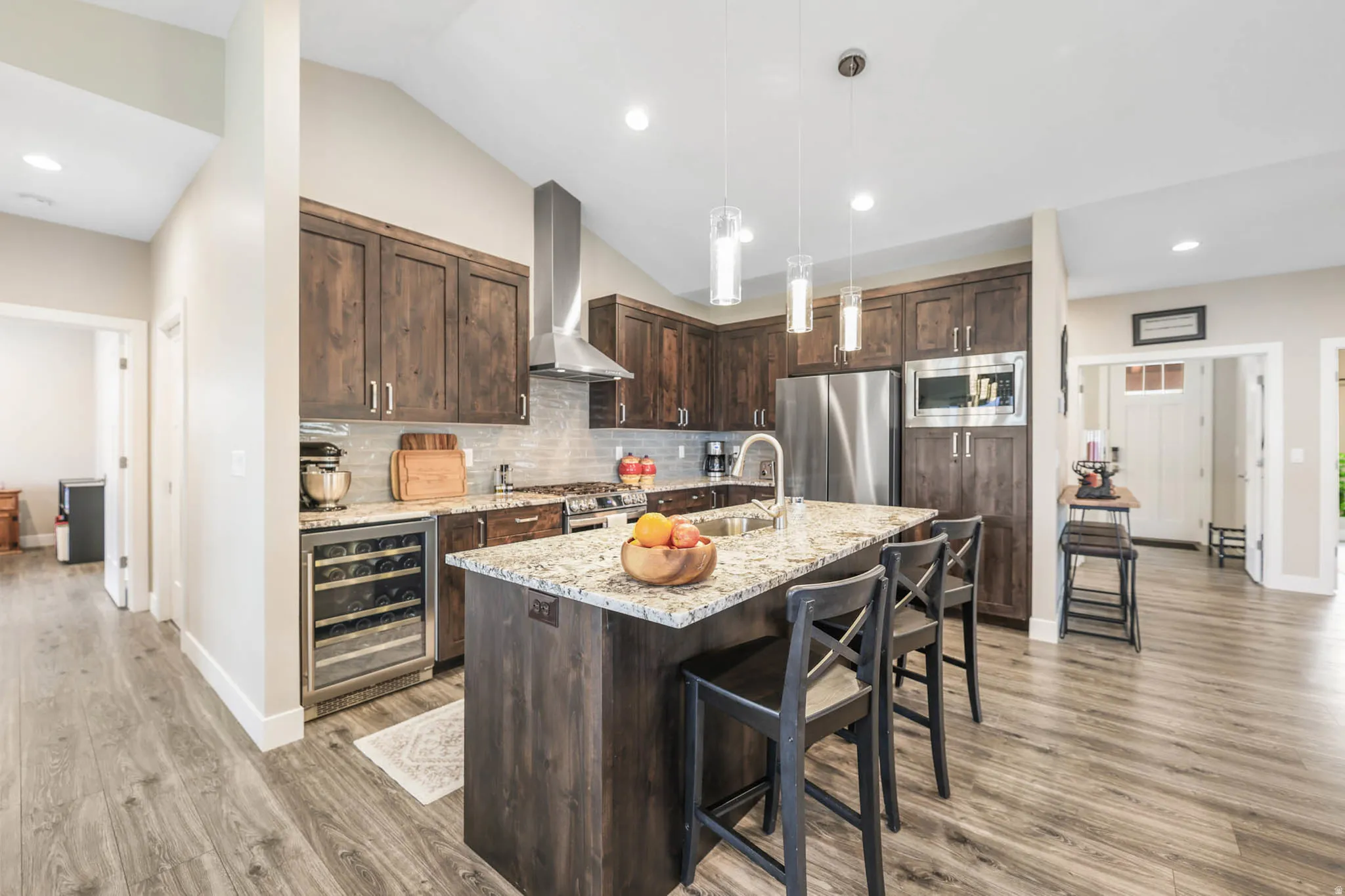 Kitchen featuring dark wood finish cabinets, light stone counters, beverage cooler, stainless steel appliances, and a kitchen bar