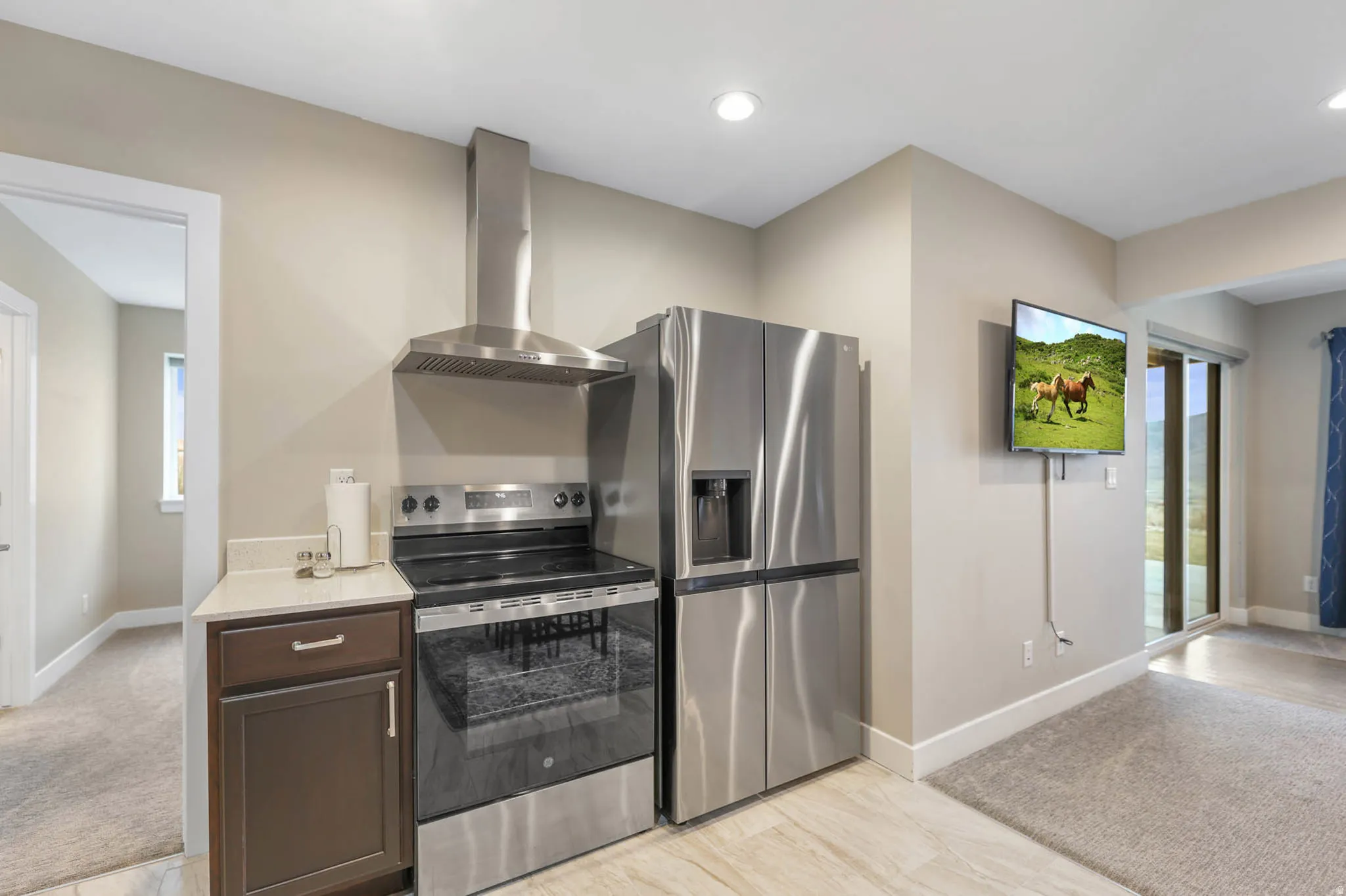 Kitchen with stainless steel appliances, light colored carpet, dark wood finish cabinetry, light stone counters, and recessed lighting