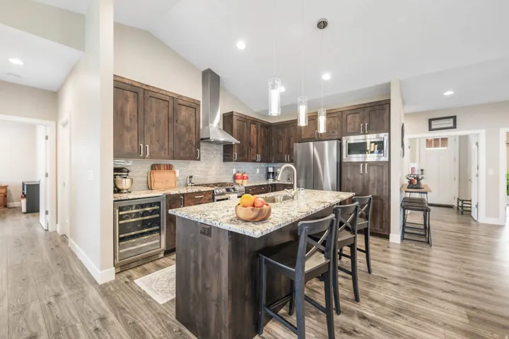 Kitchen featuring dark wood finish cabinets, light stone counters, beverage cooler, stainless steel appliances, and a kitchen bar