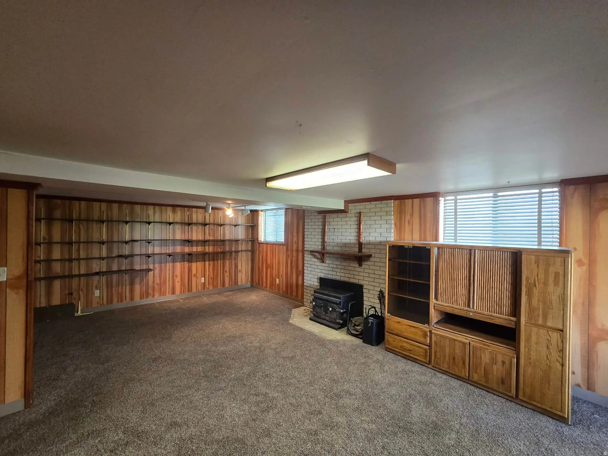 Unfurnished living room featuring wood walls, dark colored carpet, and a wood stove