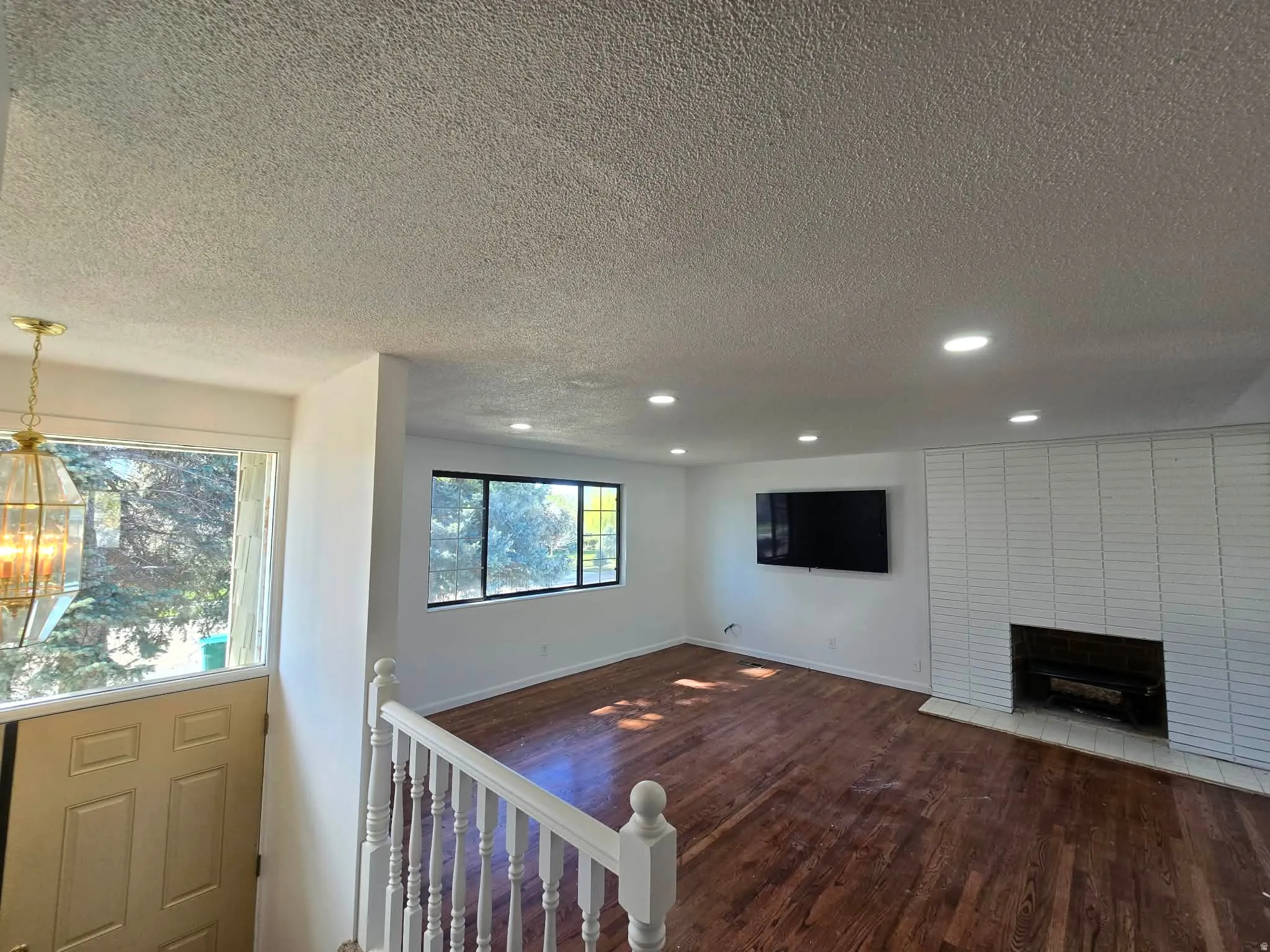 Unfurnished living room with a textured ceiling, dark wood-type flooring, a brick fireplace, and suspended lighting
