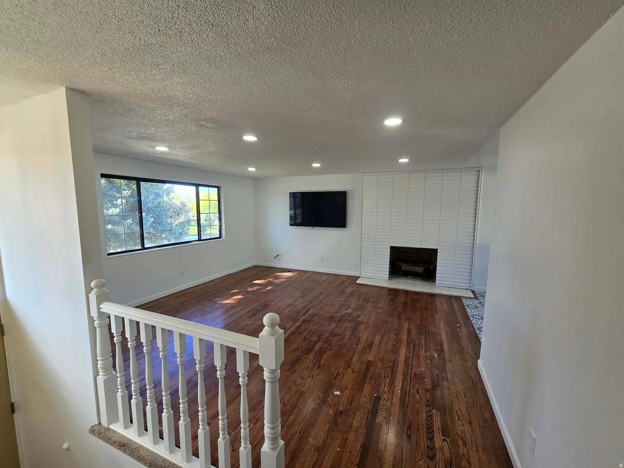 Unfurnished living room with dark wood-type flooring, a textured ceiling, recessed lighting, and a fireplace