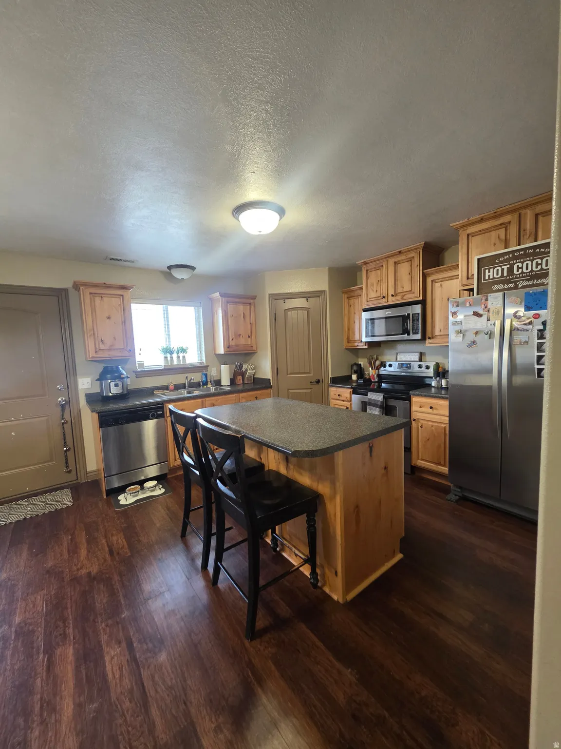 Kitchen featuring a kitchen island, dark countertops, stainless steel appliances, a breakfast bar area, and dark wood-type flooring