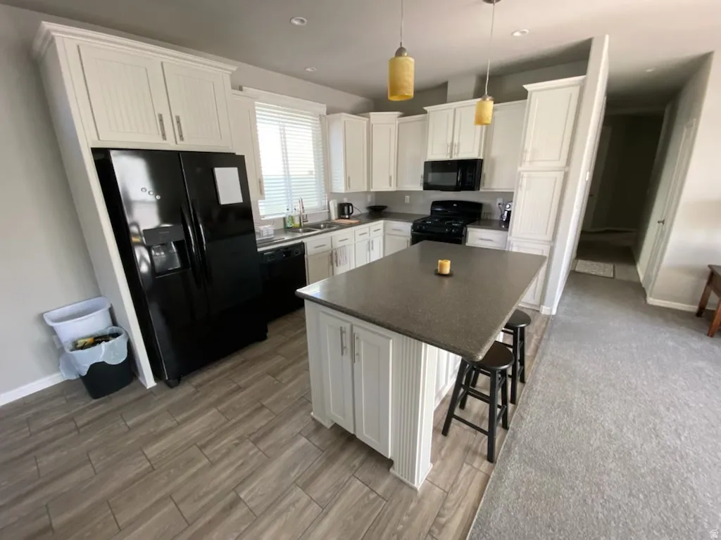 Kitchen with white cabinetry, black appliances, a kitchen bar, wood finish floors, and a center island