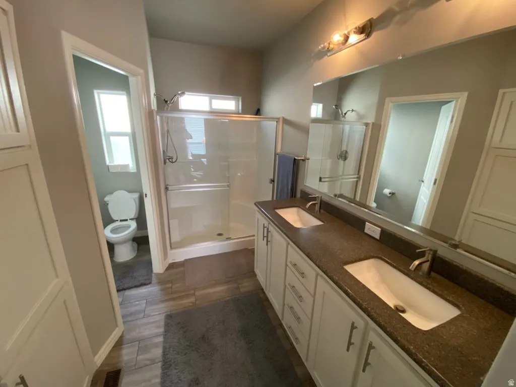 Full bathroom featuring double vanity, a stall shower, water closetand dark wood finished floors