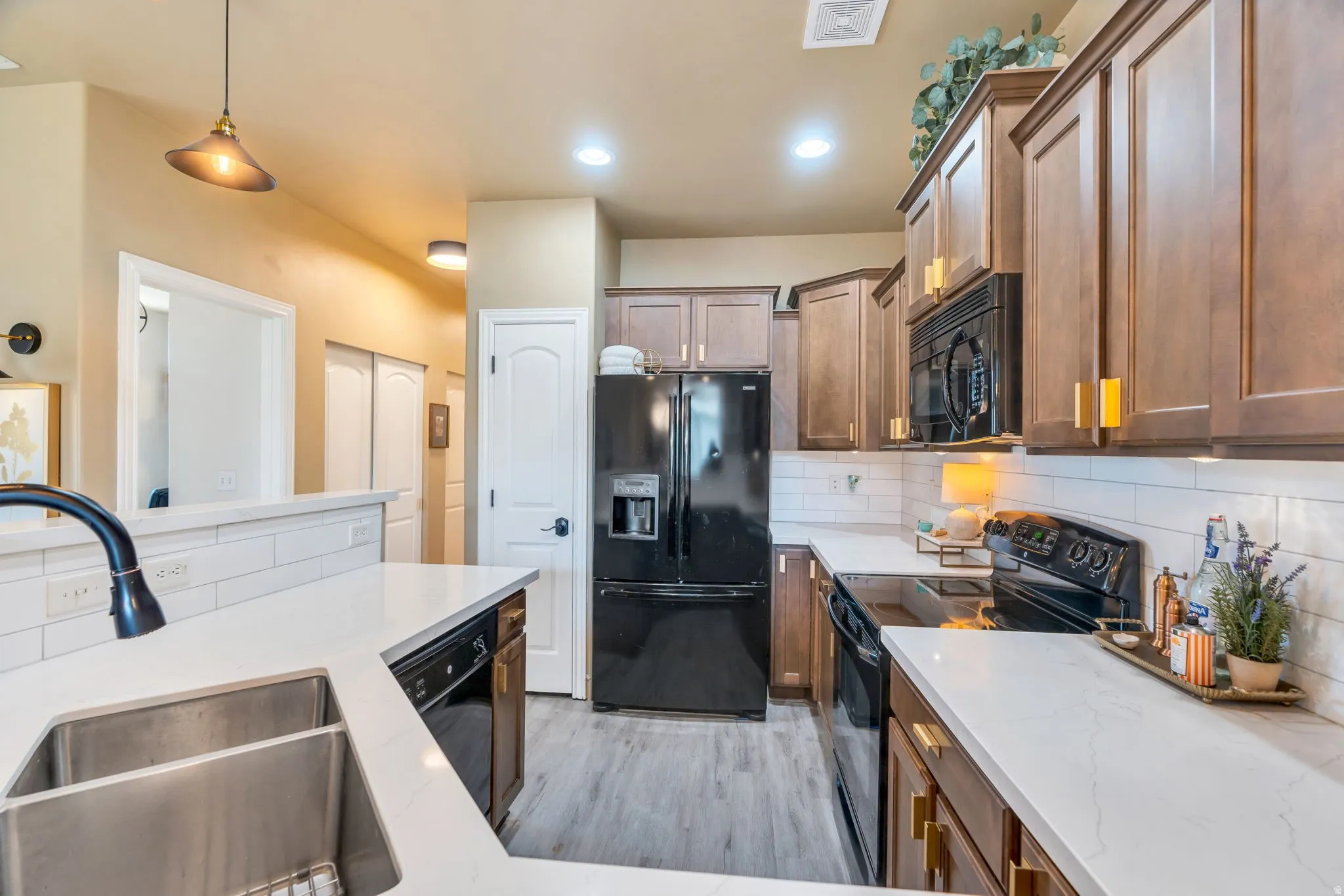 Kitchen with black appliances, tasteful backsplash, pendant lighting, light stone countertops, and light wood-style floors