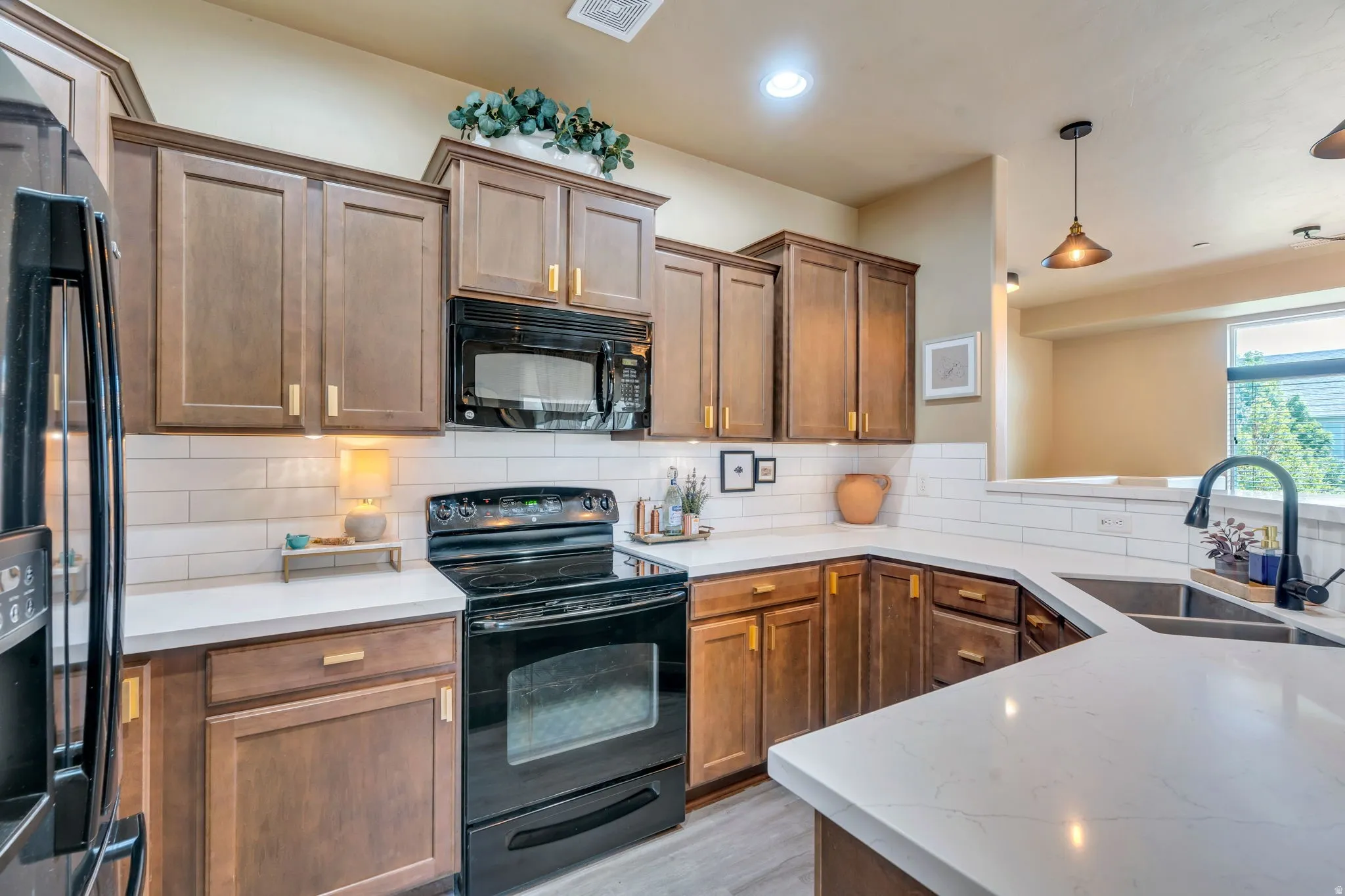 Kitchen with black appliances, hanging light fixtures, wood finish cabinets, tasteful backsplash, and light stone countertops