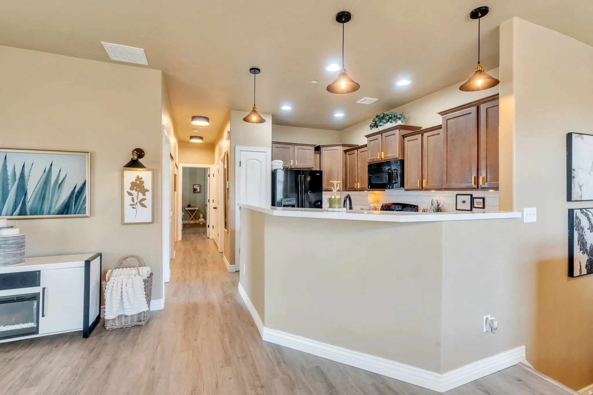 Kitchen featuring black appliances, light countertops, pendant lighting, a peninsula, and light wood-type flooring
