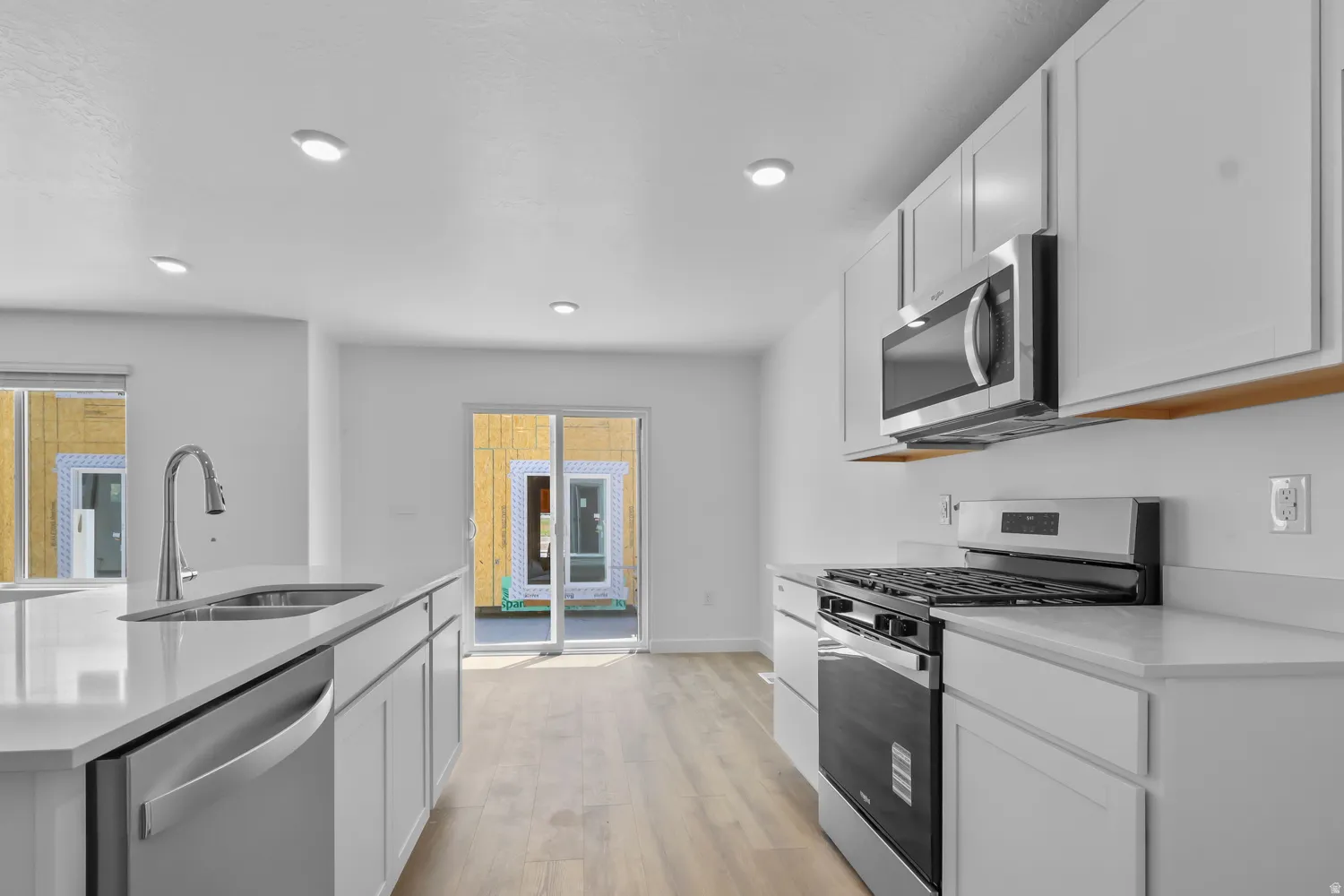 Kitchen with stainless steel appliances, light wood-style floors, white cabinets, light stone countertops, and an island with sink