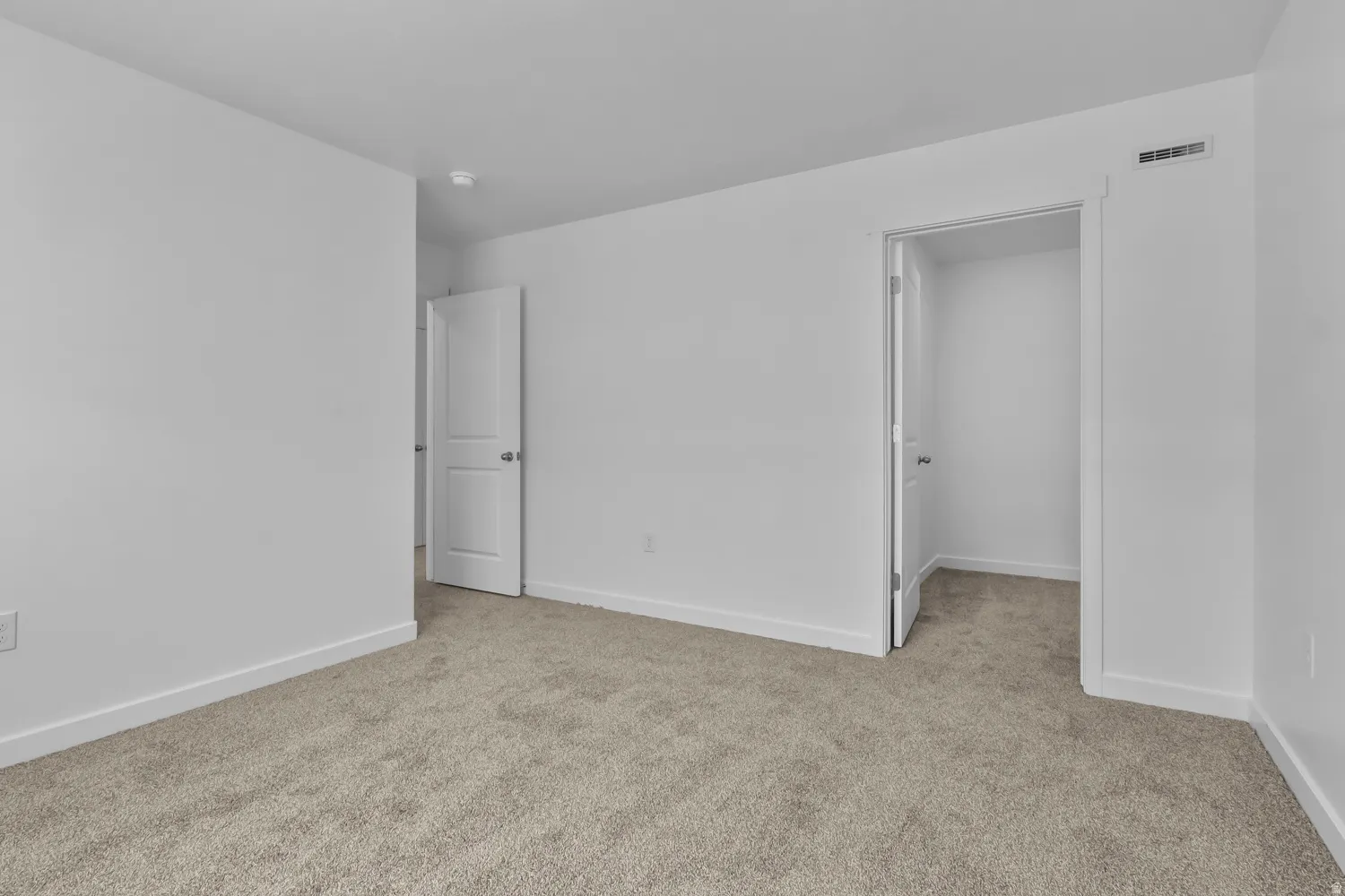 Unfurnished bedroom with light colored carpet and a walk in closet