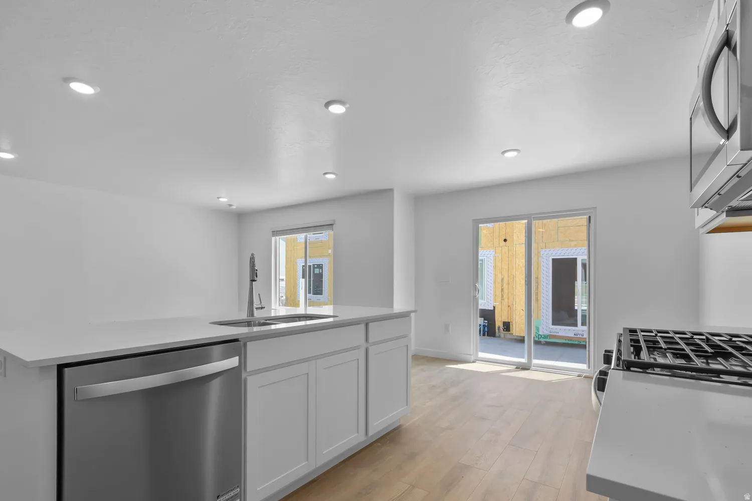 Kitchen featuring stainless steel appliances, light wood-style flooring, a kitchen island with sink, recessed lighting, and white cabinetry