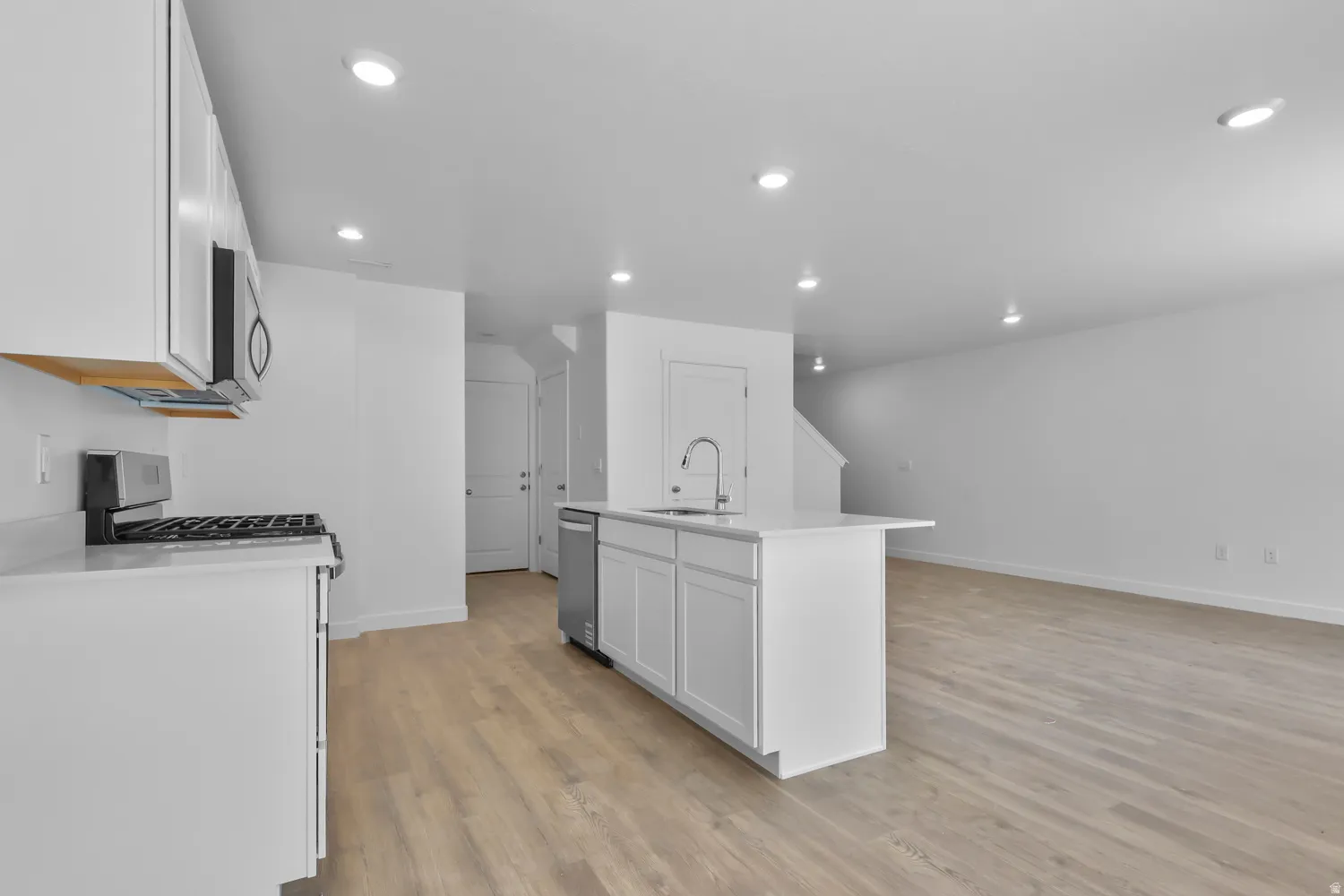 Kitchen featuring an island with sink, white cabinets, light wood-style flooring, stainless steel appliances, and recessed lighting