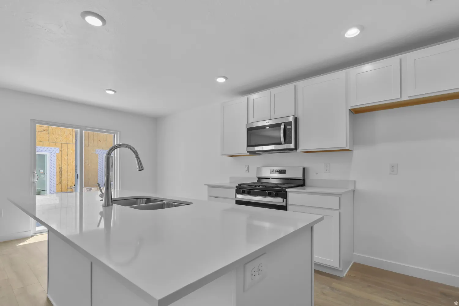 Kitchen featuring stainless steel appliances, white cabinets, light wood-style flooring, a center island with sink, and recessed lighting