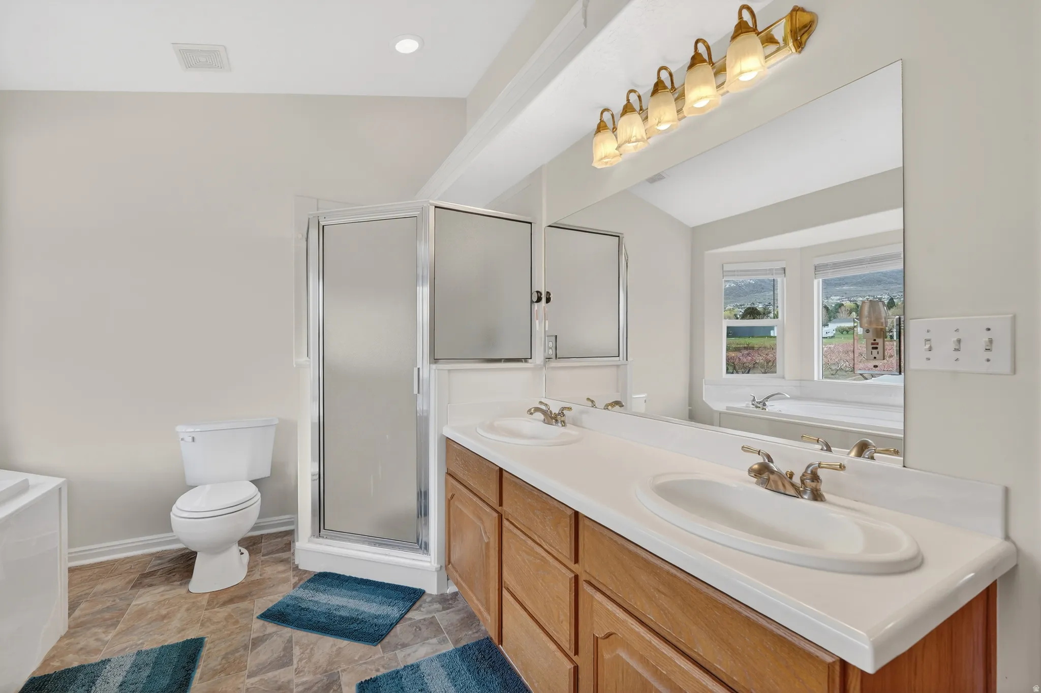 Full bath featuring a garden tub, double vanity, a stall shower, vaulted ceiling, and light stone finish flooring