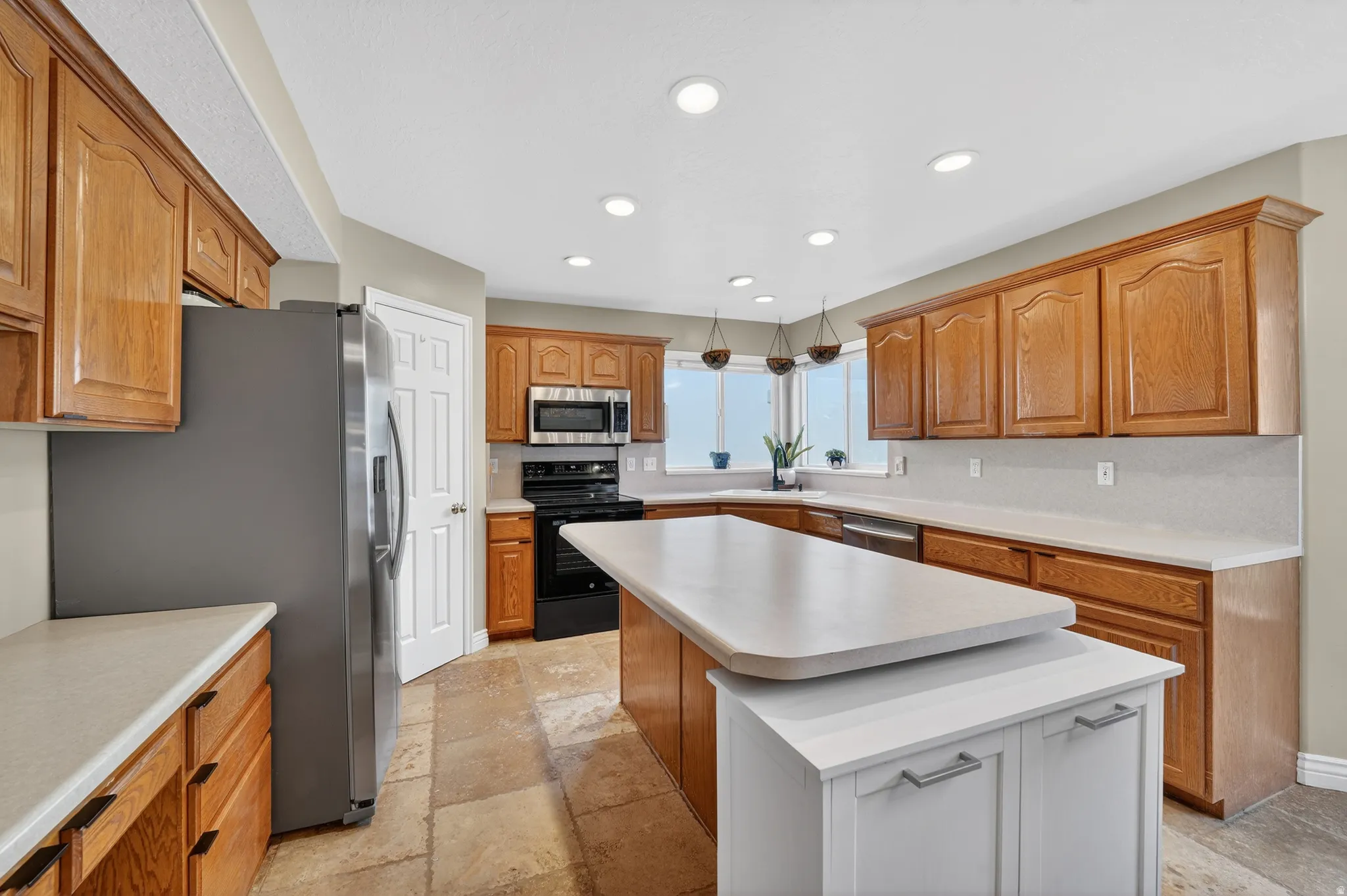 Kitchen with stainless steel appliances, light countertops, wood finish cabinetry, a kitchen island, and recessed lighting