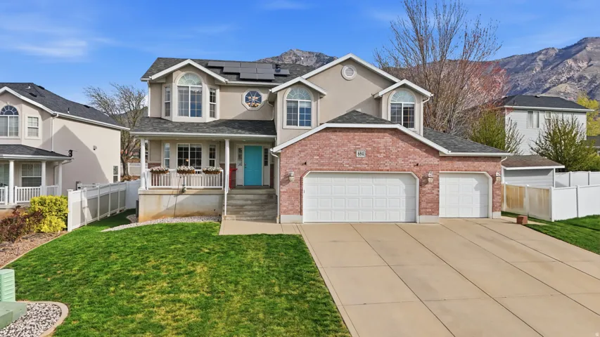 Traditional-style house with a garage, covered porch, solar panels, driveway, and brick siding