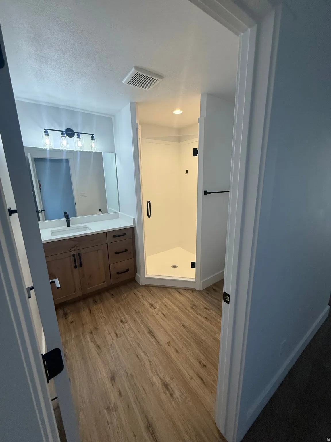 Bathroom with vanity, light wood-type flooring, a stall shower, and a textured ceiling