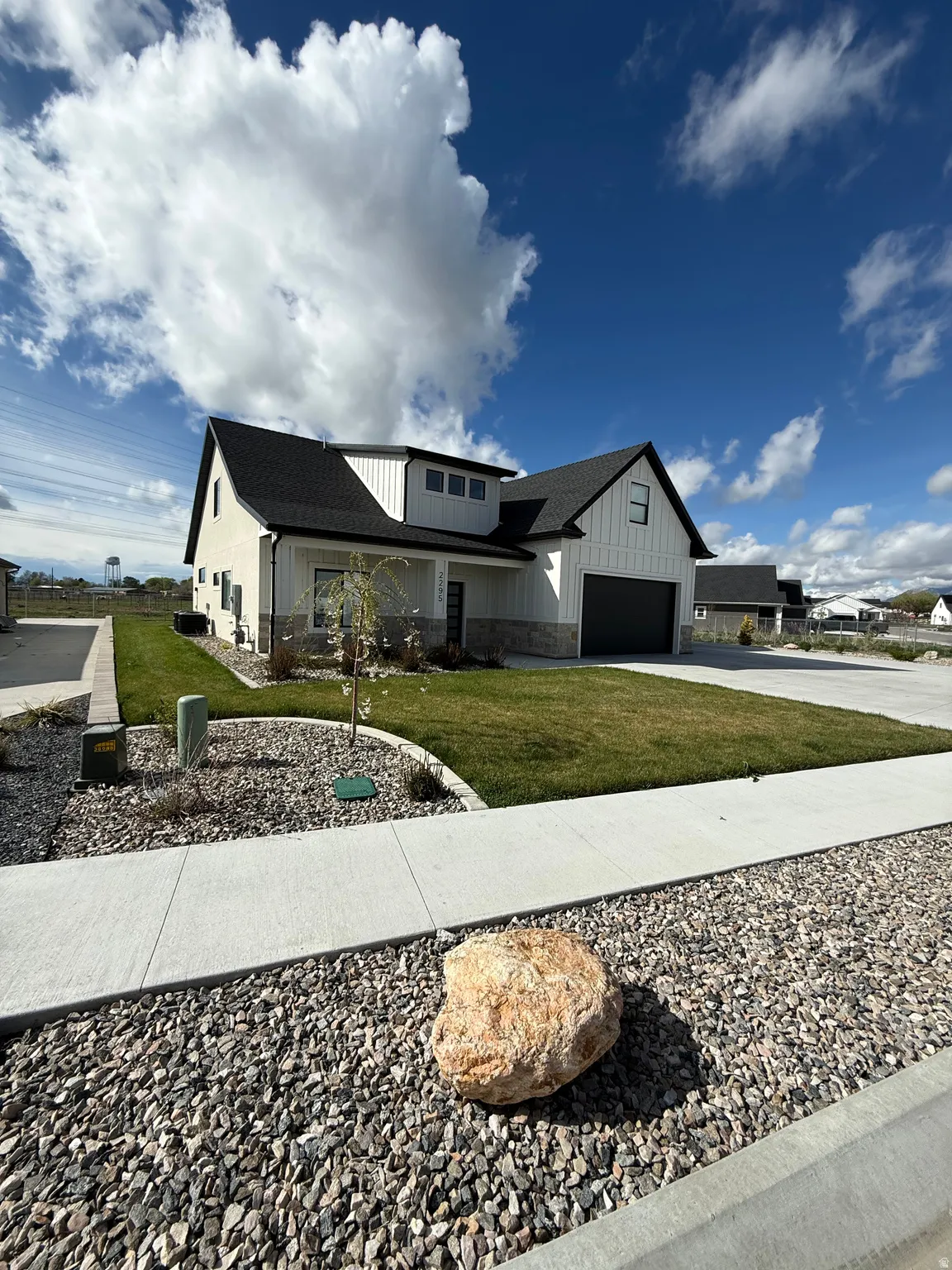 Modern farmhouse with board and batten siding, driveway, stone siding, a shingled roof, and a front lawn