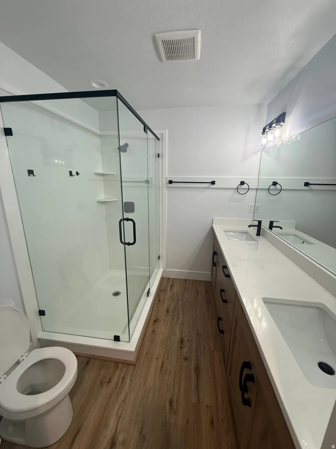 Bathroom with dark wood-style flooring, double vanity, a shower stall, and a textured ceiling