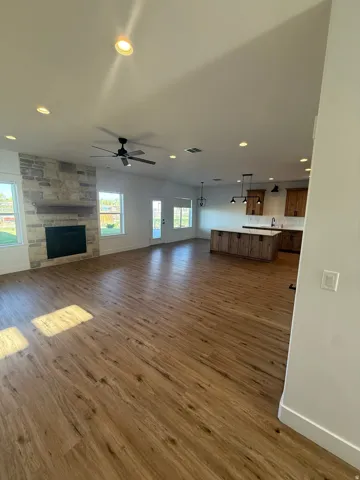 Unfurnished living room with a stone fireplace, recessed lighting, dark wood-type flooring, and a ceiling fan