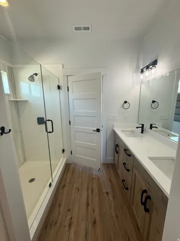 Bathroom with a stall shower, dark wood-style flooring, and double vanity
