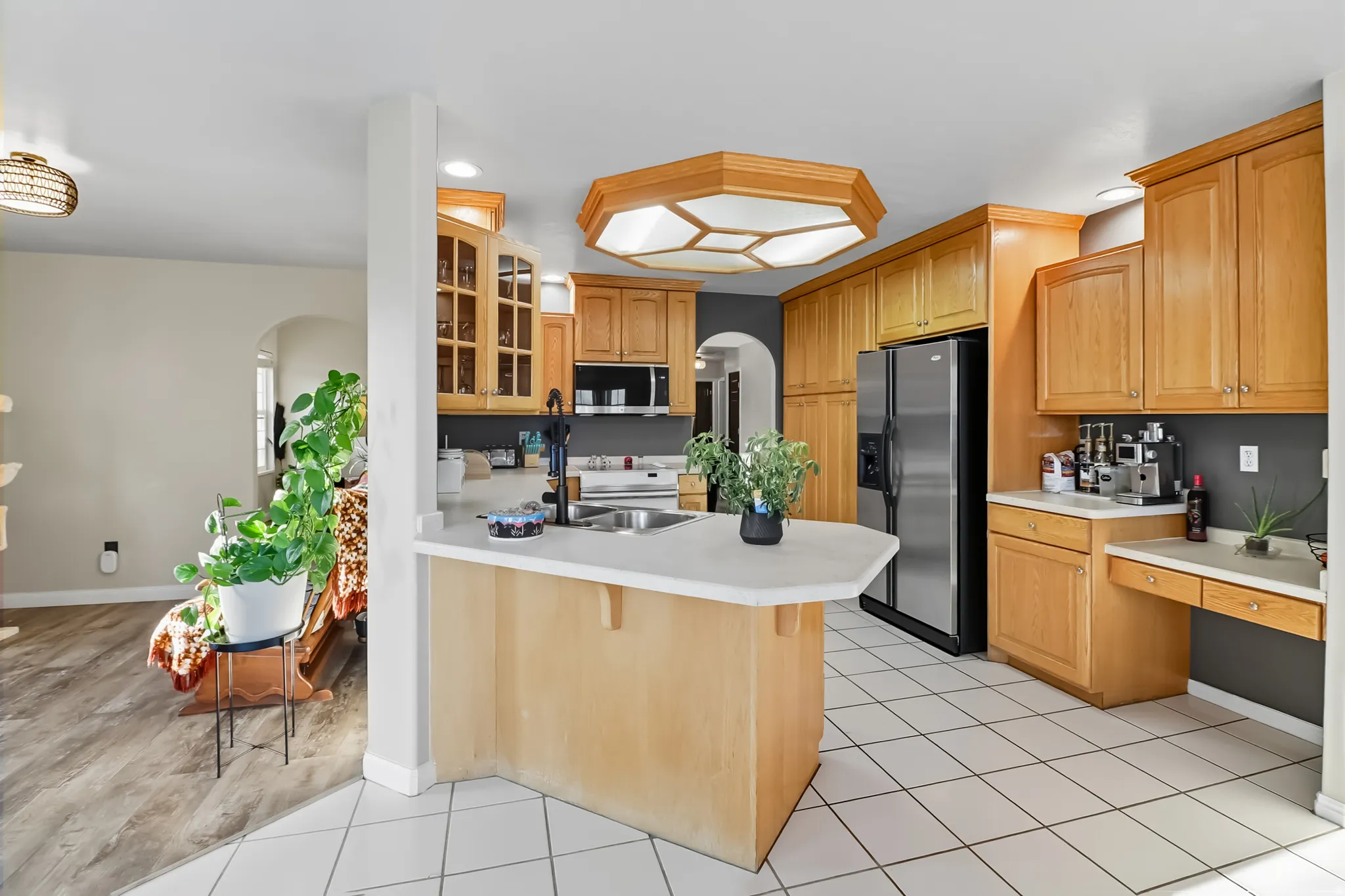 Kitchen featuring arched walkways, appliances, glass fronted cabinets, a peninsula, and light countertops