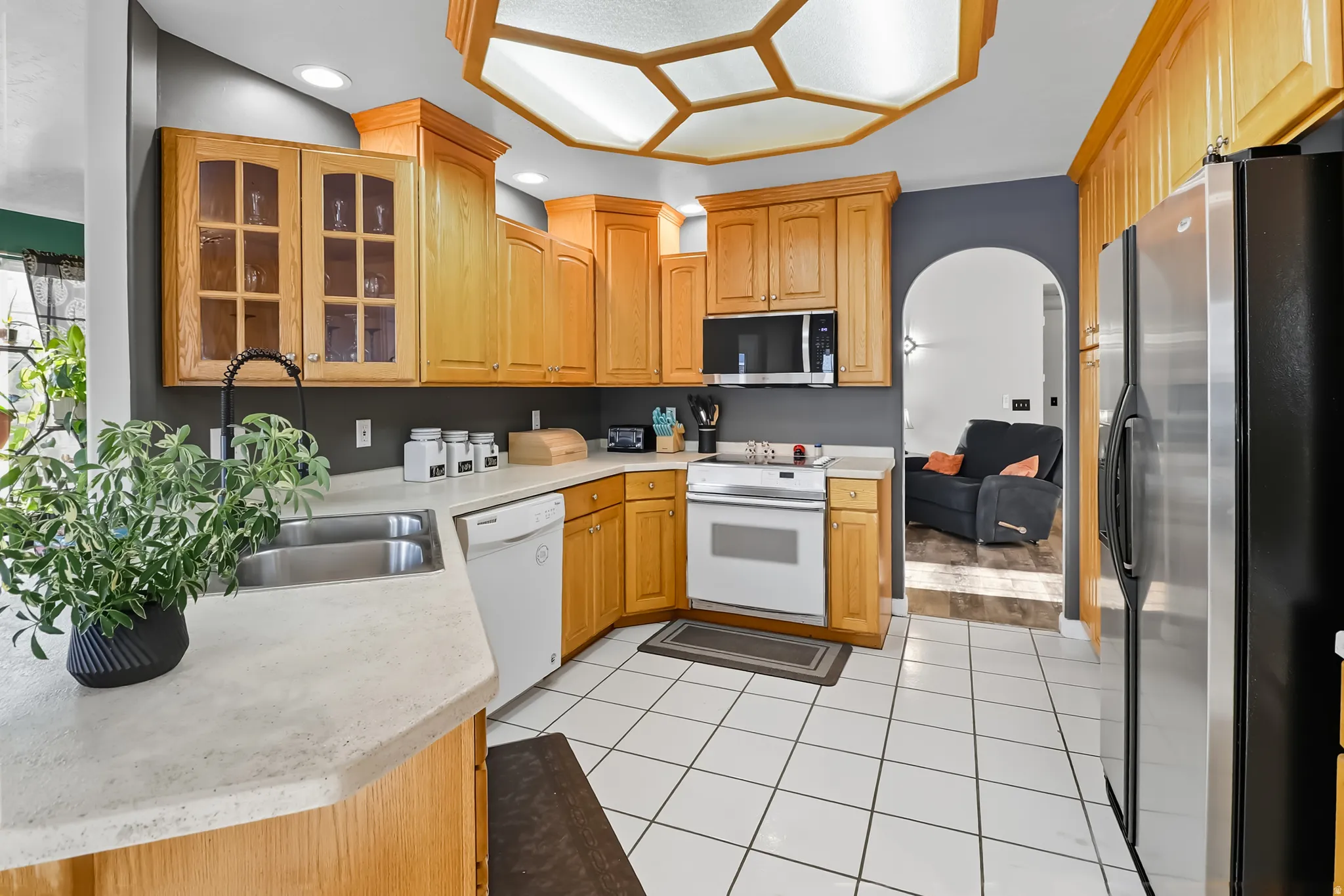 Kitchen featuring arched walkways, appliances, glass fronted cabinets, and light tile patterned flooring