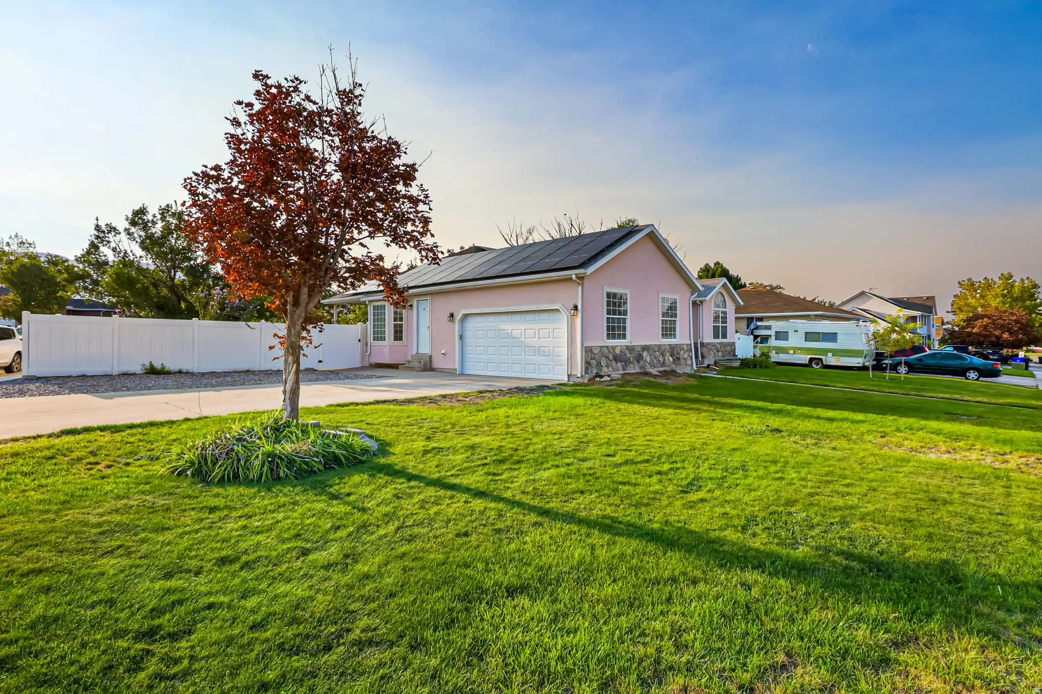 Rambler style house featuring roof mounted solar panels, stucco siding, concrete driveway, stone siding, and a garage