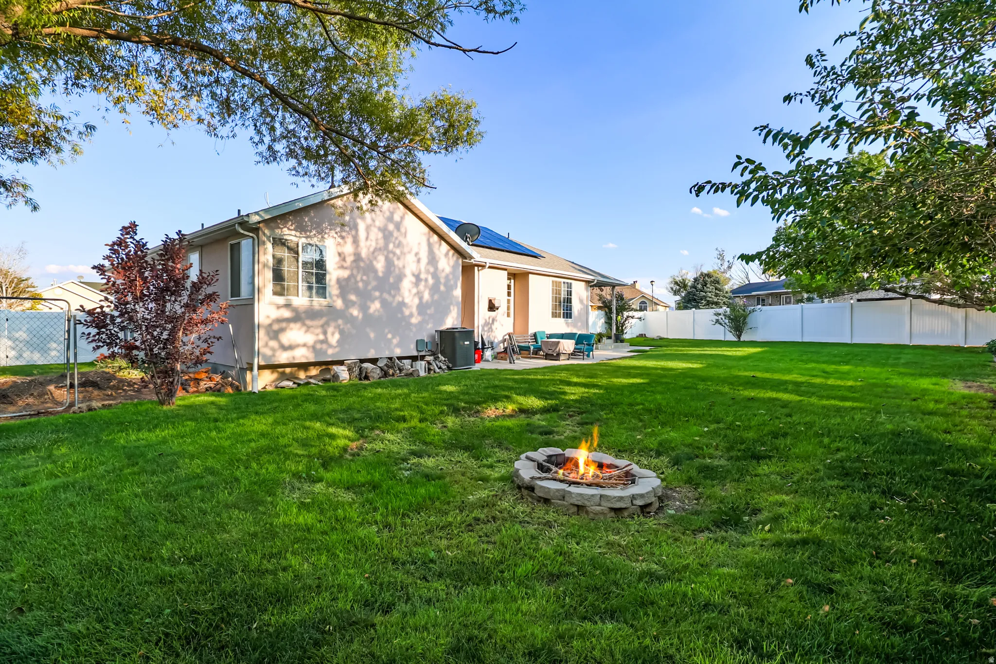 Back of property featuring a fenced backyard, a patio area, solar panels, and an outdoor living space with a fire pit