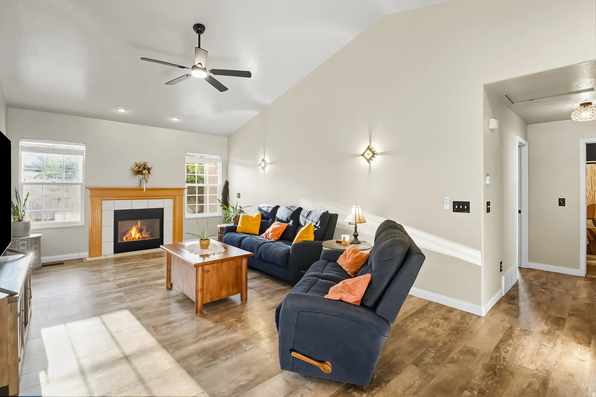 Living area with vaulted ceiling, a tiled fireplace, light wood-type flooring, and a ceiling fan