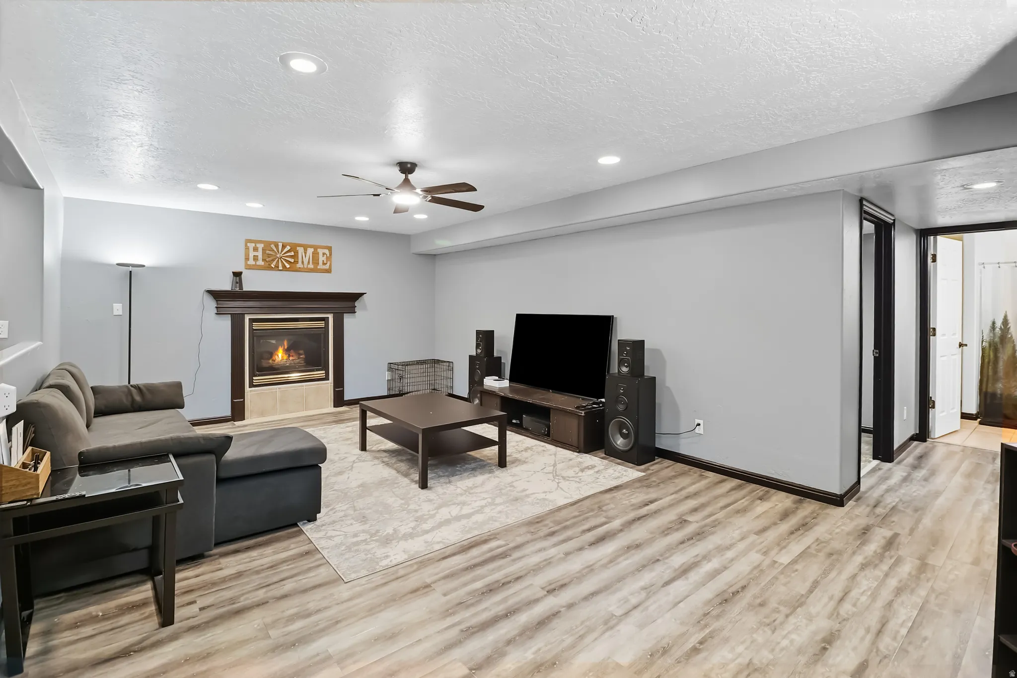 Basement living room featuring a tile fireplace, light wood-style flooring, ceiling fan, a textured ceiling, and recessed lighting