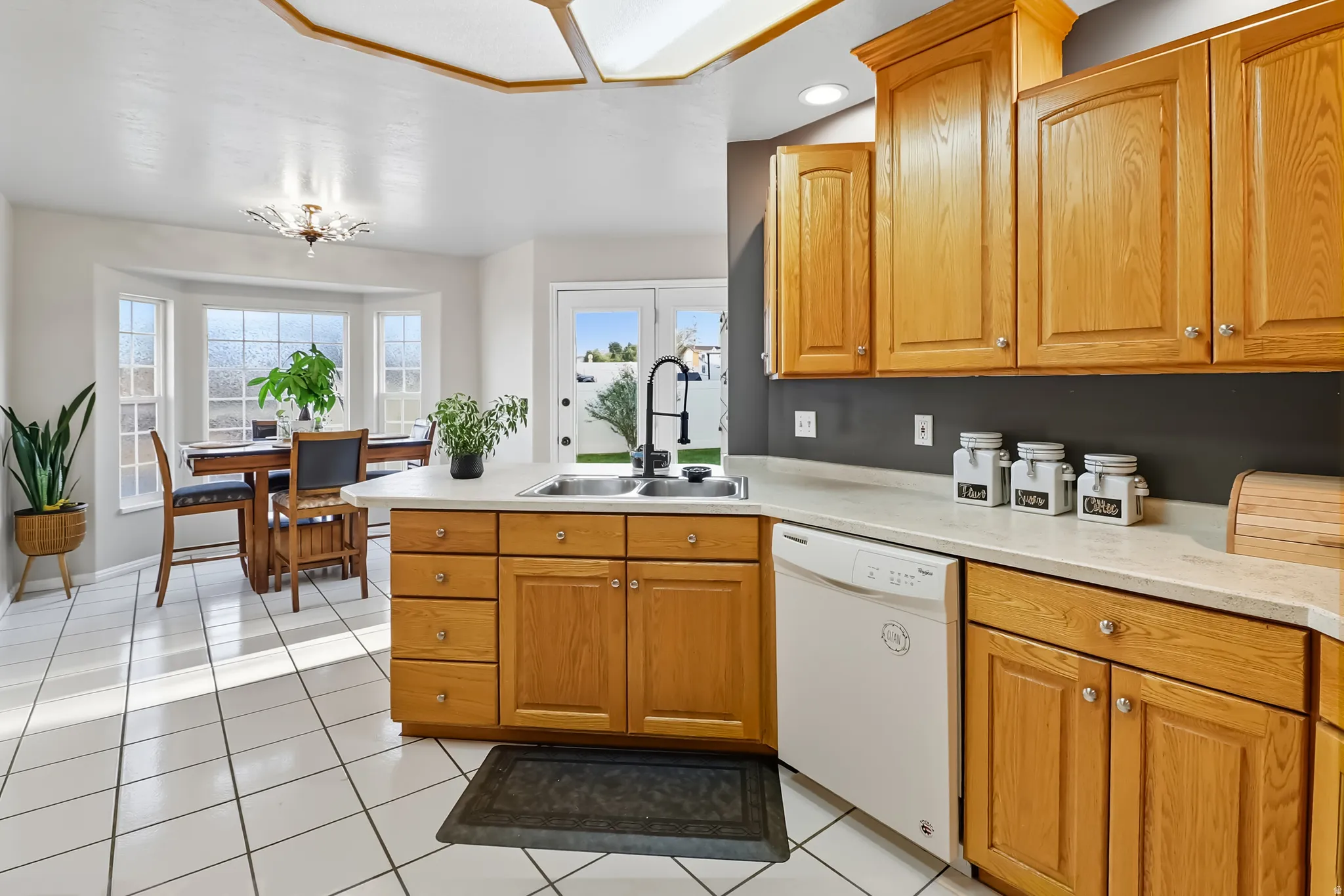Kitchen with light countertops, a peninsula, white dishwasher, light tile patterned floors, and wood finish cabinetry