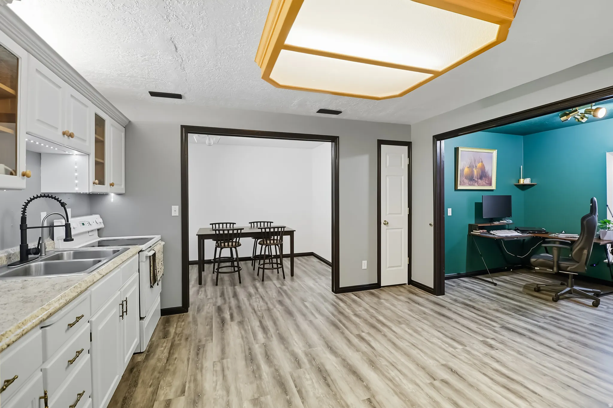 Basement kitchen with white cabinetry, a desk, light wood-style flooring, light countertops, and a textured ceiling