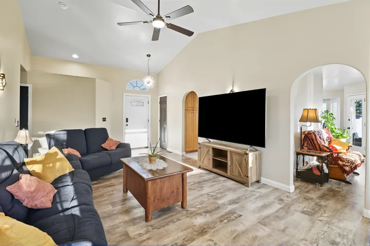 Living room featuring arched walkways, light wood finished floors, ceiling fan, lofted ceiling, and suspended lighting