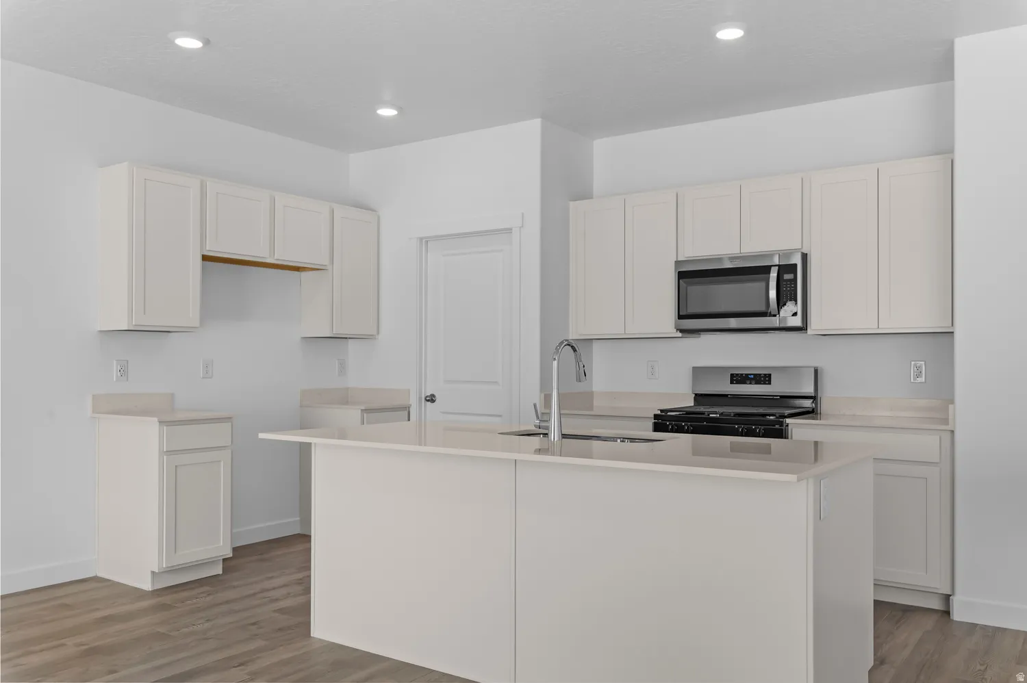 Kitchen featuring an island with sink, stainless steel appliances, light wood-type flooring, white cabinets, and recessed lighting