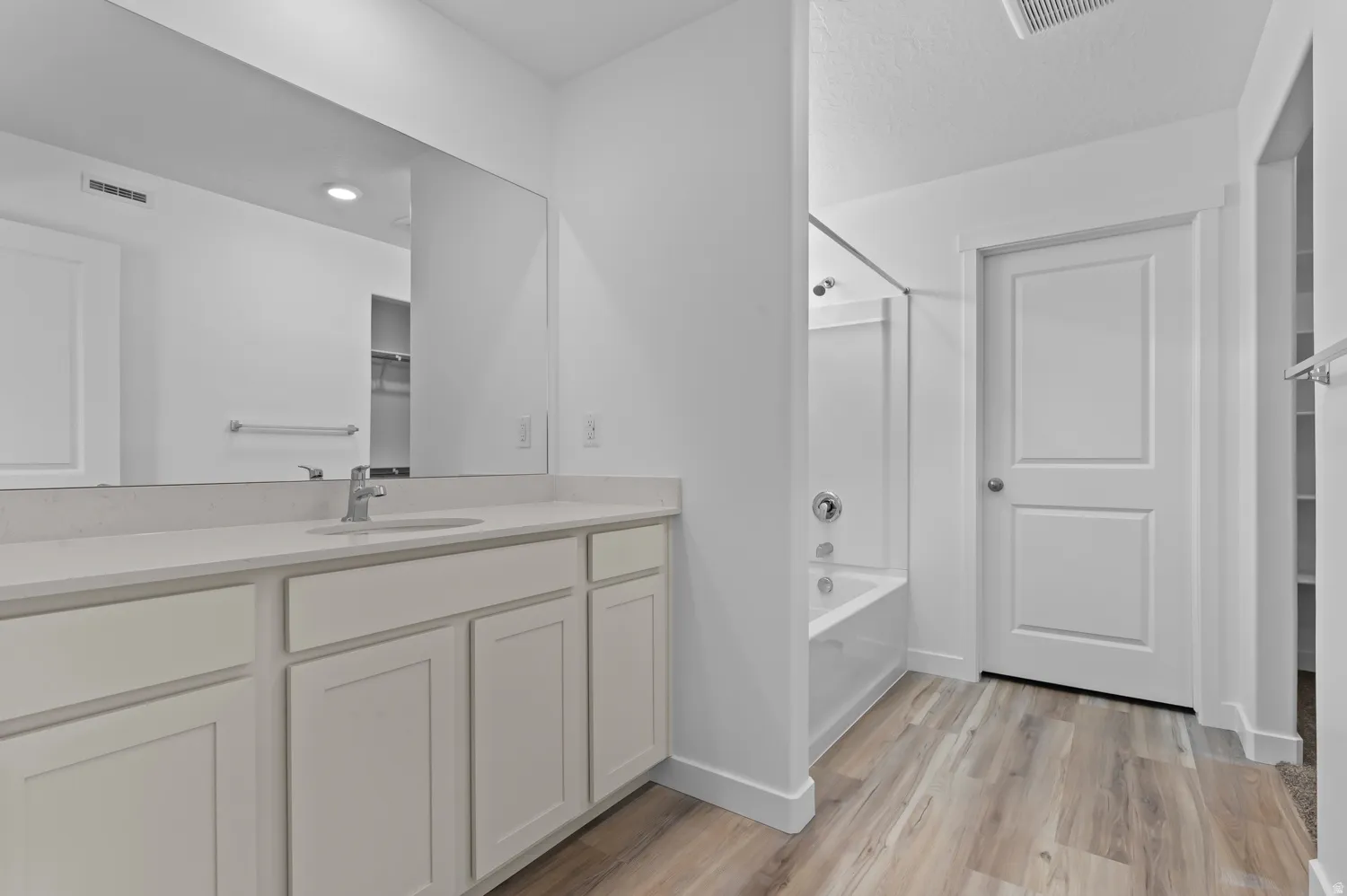 Bathroom with a spacious closet, vanity, light wood finished floors, and  shower combination