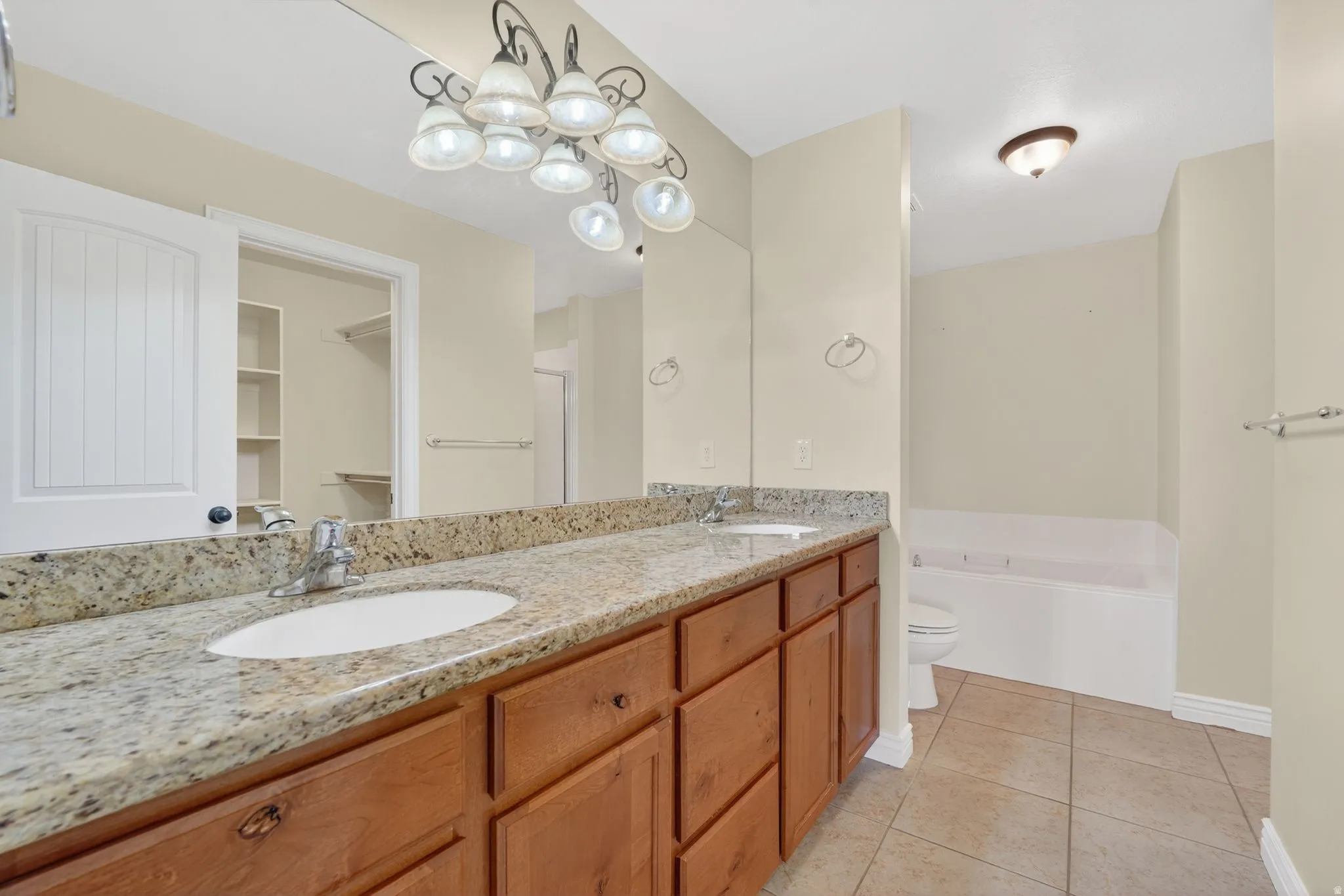 Full bath with double vanity, light tile patterned floors, a bath, and a walk in closet