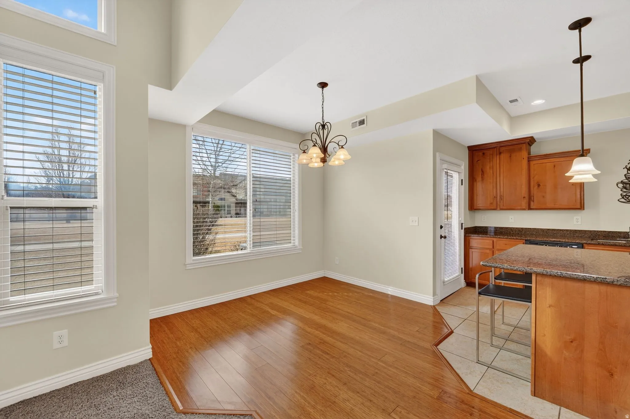Kitchen featuring dark stone counters, hanging lights, wood finish cabinets, light wood-type flooring, and a breakfast bar area