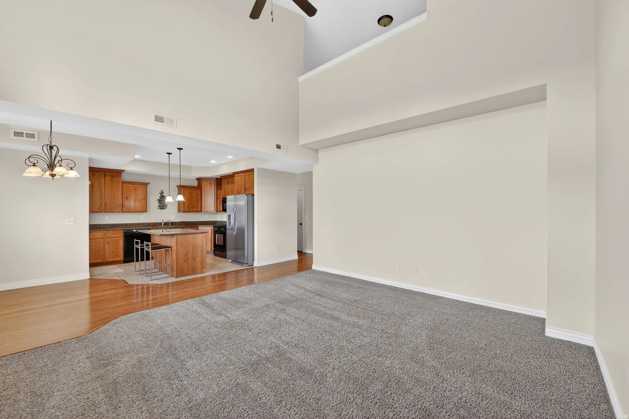 Living area with light colored carpet, suspended lighting, a ceiling fan, and a high ceiling