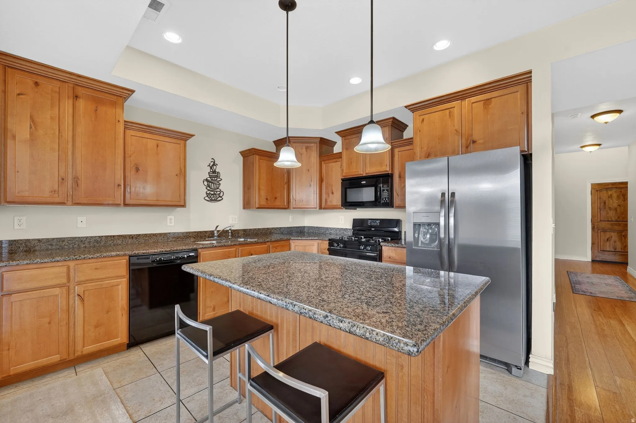 Kitchen featuring black appliances, a kitchen bar, dark stone countertops, a kitchen island, and hanging light fixtures