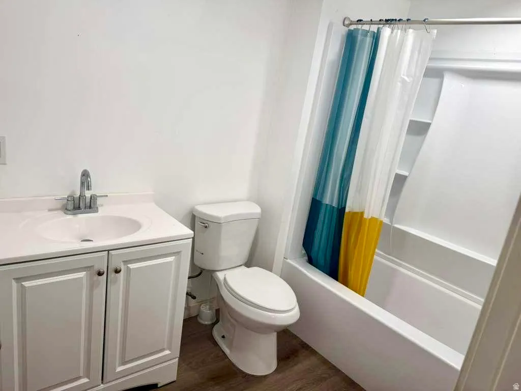 Full bathroom with vanity, dark wood-style floors, and shower / bath combo with shower curtain