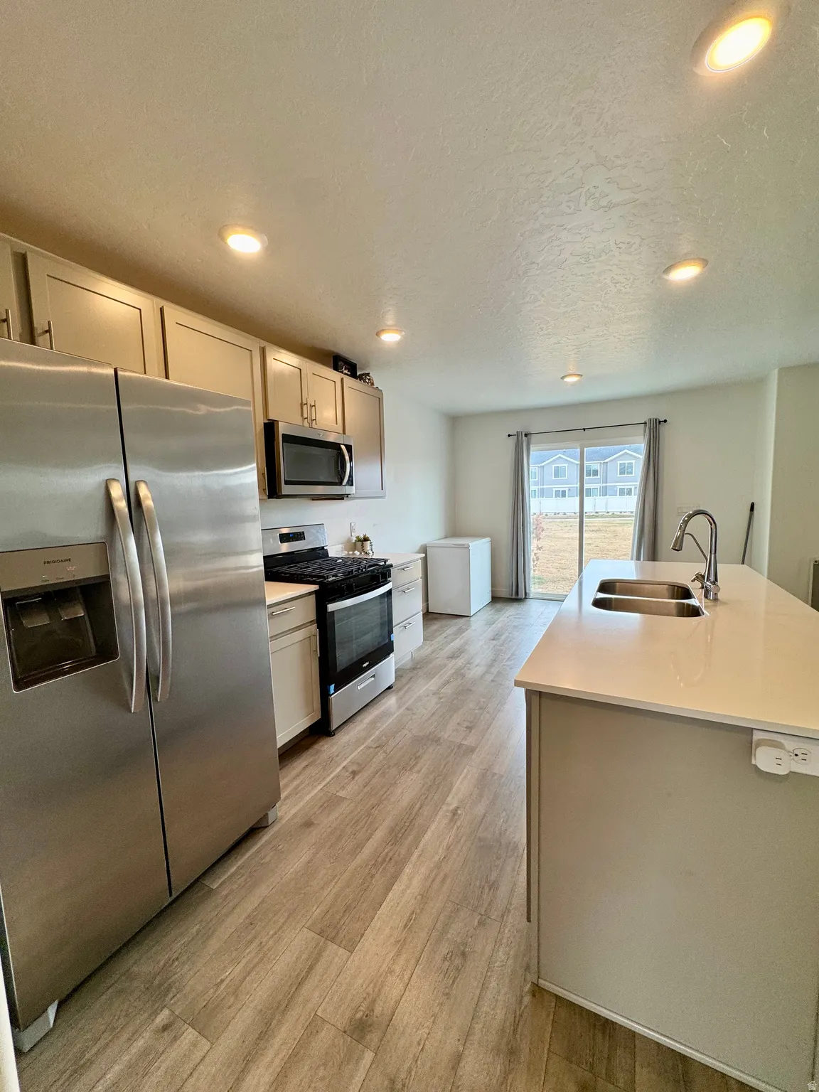 Kitchen featuring stainless steel appliances, a textured ceiling, a kitchen island with sink, recessed lighting, and light wood-style flooring