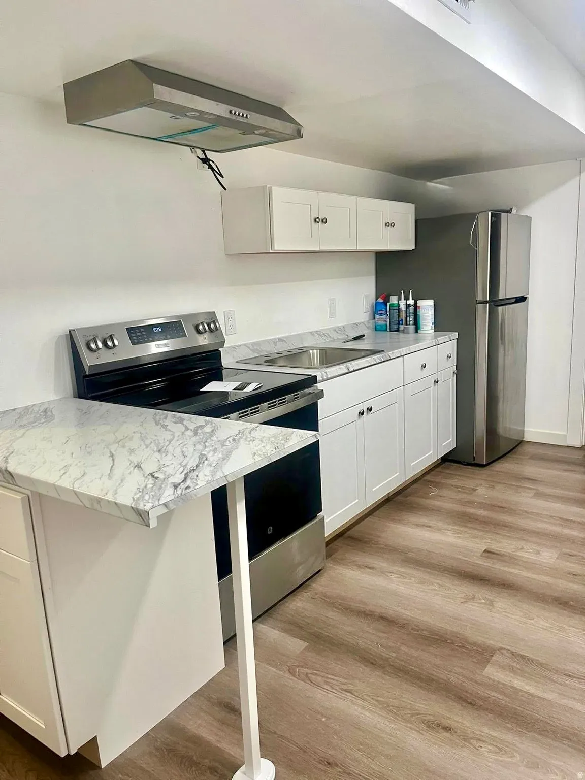 Kitchen featuring stainless steel appliances, light wood-style flooring, white cabinets, ventilation hood, and a peninsula