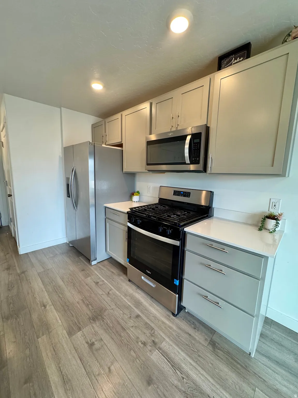 Kitchen with stainless steel appliances, light wood finished floors, gray cabinetry, and recessed lighting