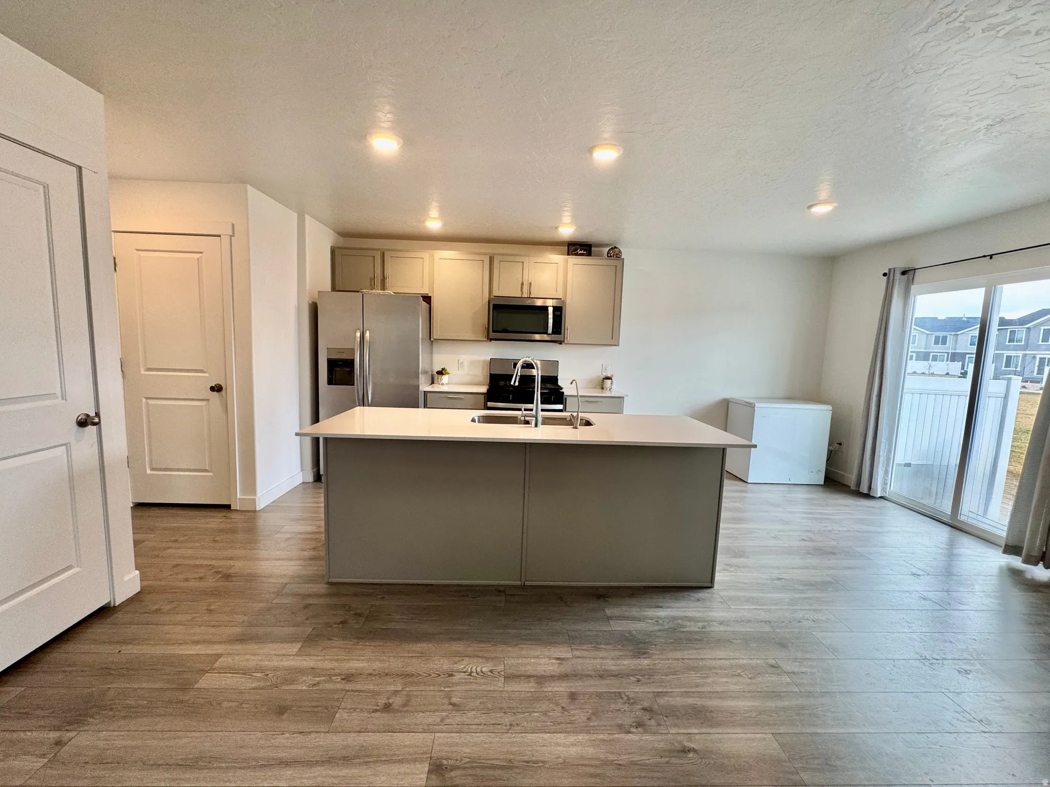 Kitchen featuring a center island with sink, a textured ceiling, gray cabinetry, dark wood-style floors, and stainless steel appliances