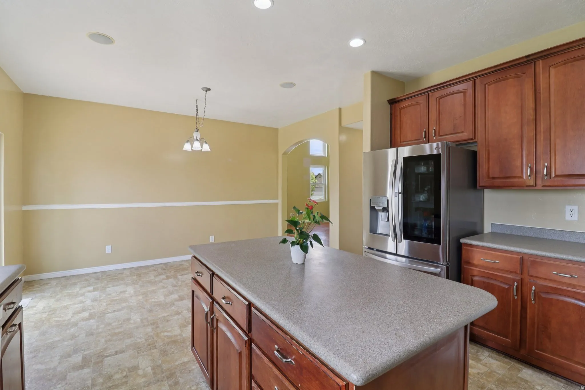 Kitchen featuring stainless steel fridge, a center island, arched walkways, pendant lighting, and light countertops