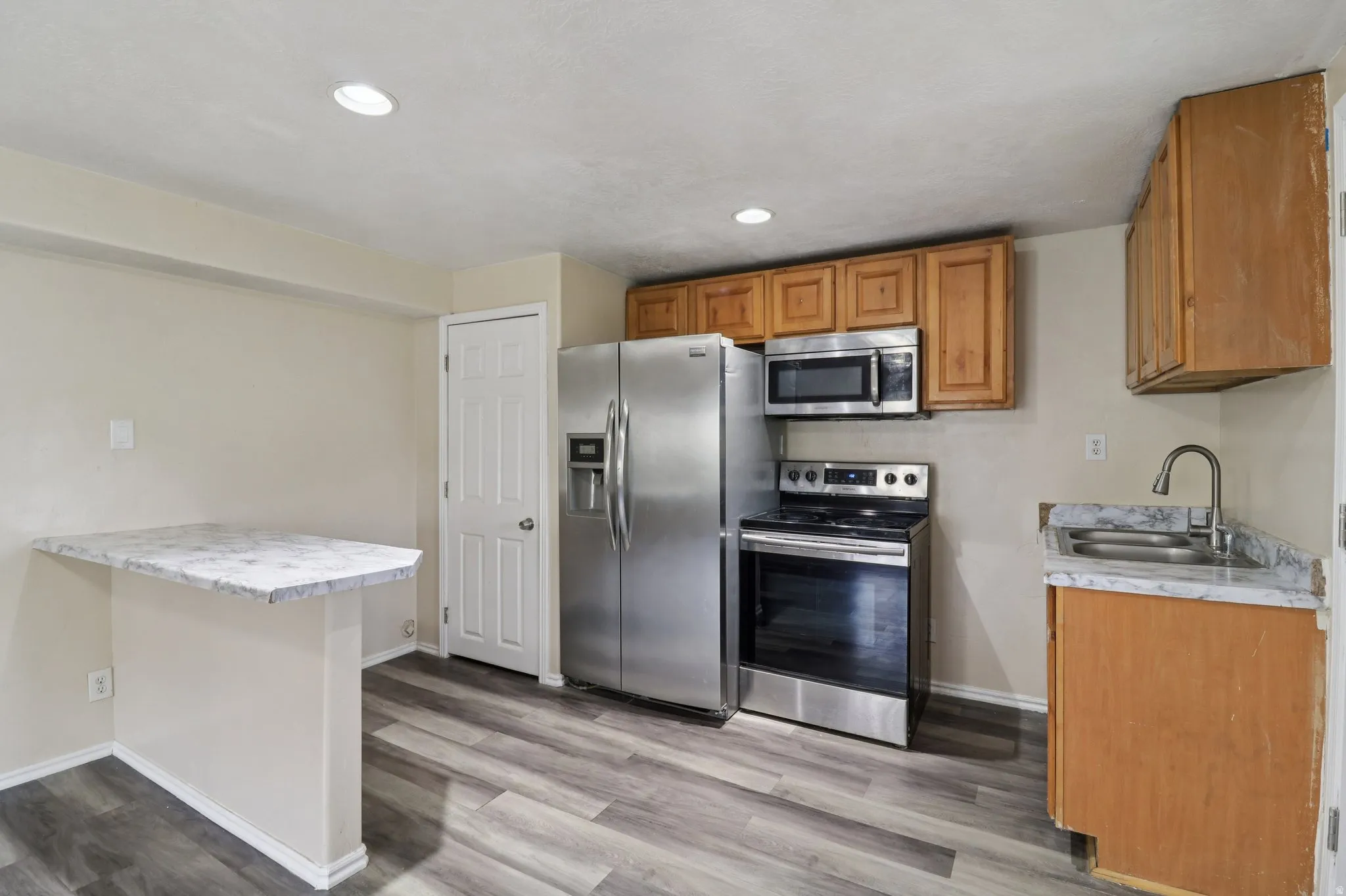 Kitchen with stainless steel appliances, light countertops, a peninsula, a breakfast bar area, and light wood-style flooring