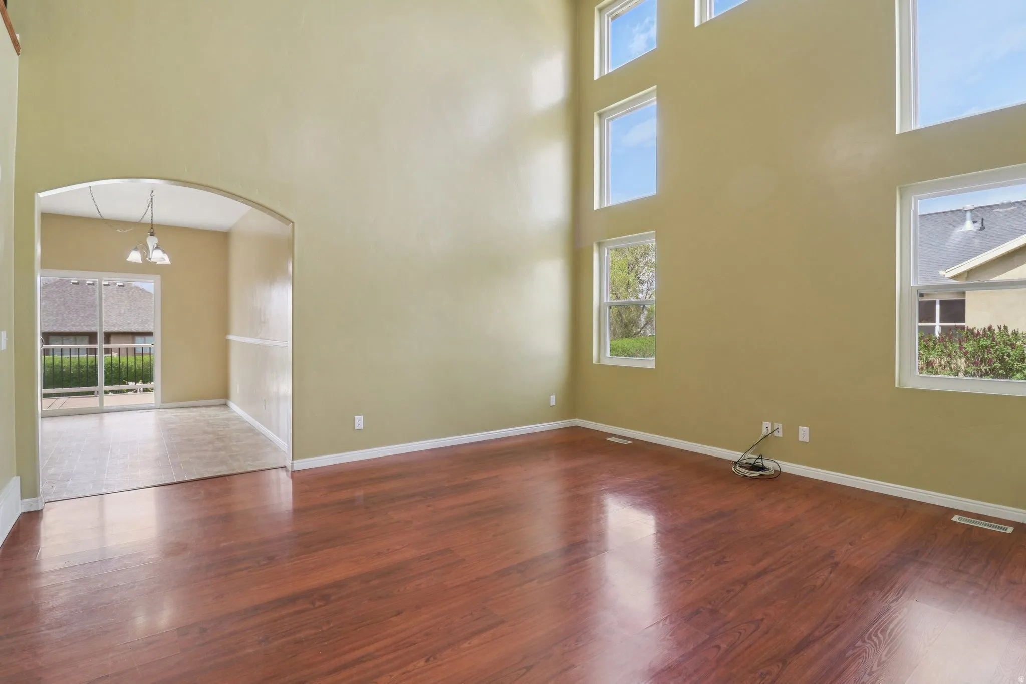 Empty room with arched walkways, a high ceiling, wood finished floors, and hanging lights