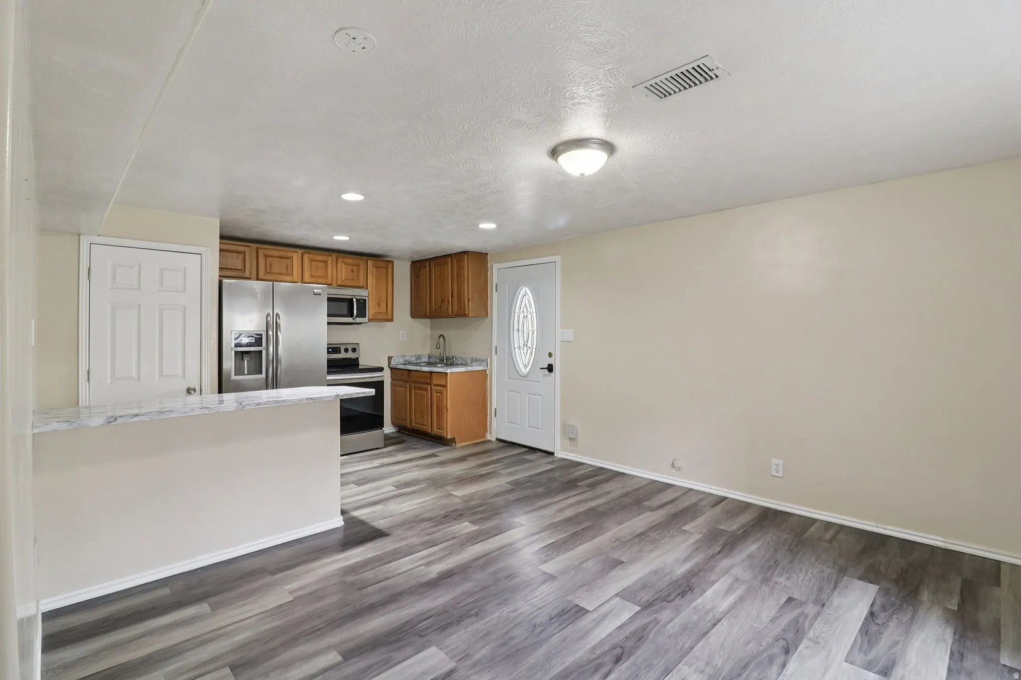 Kitchen with wood finish cabinetry, stainless steel appliances, dark wood finished floors, recessed lighting, and a textured ceiling