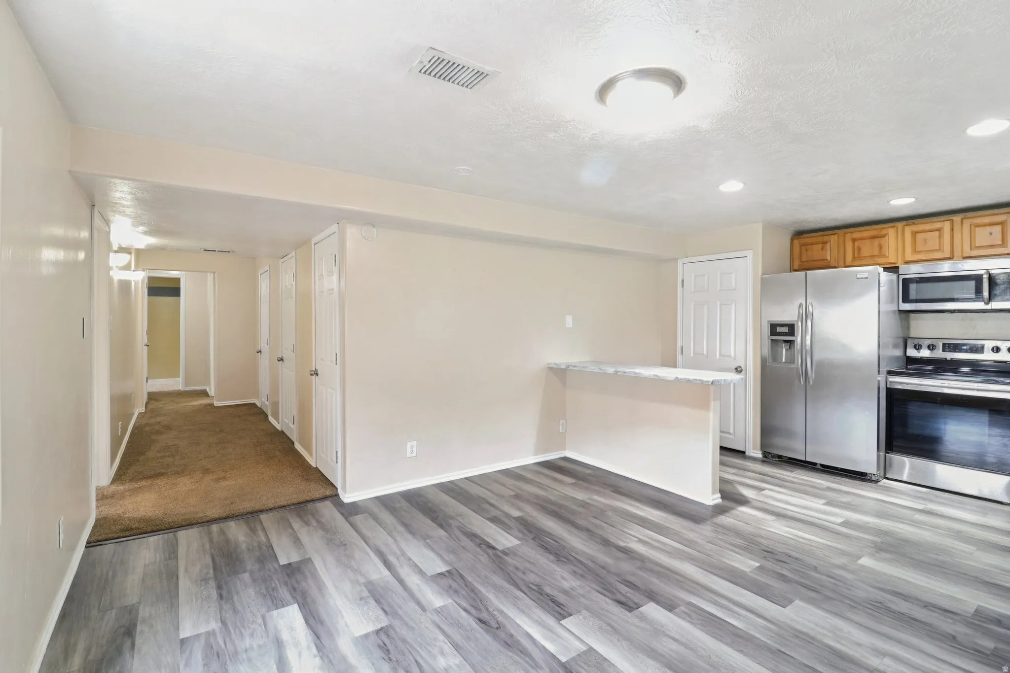 Kitchen with stainless steel appliances, a peninsula, light wood-style floors, recessed lighting, and wood finish cabinetry